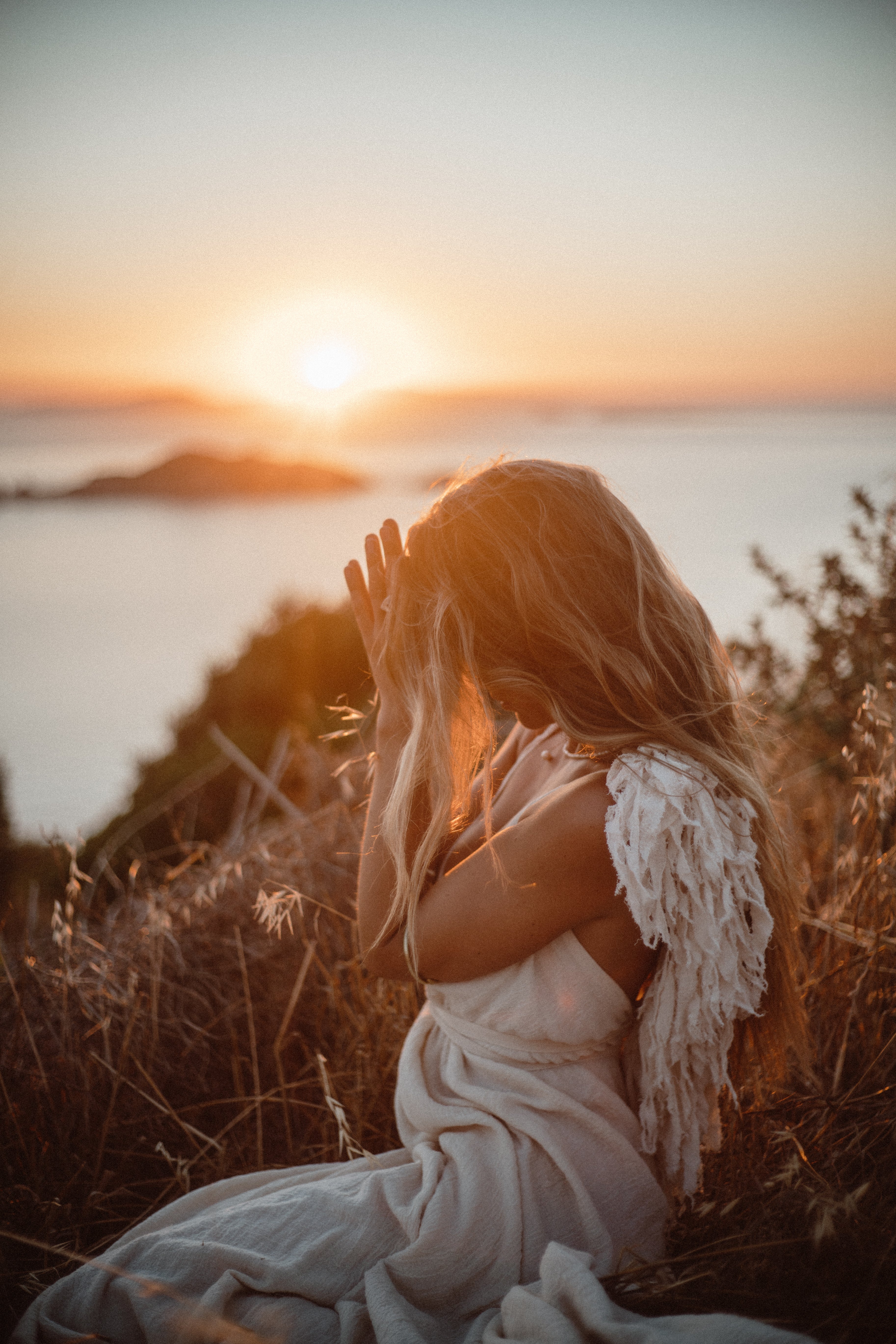 Woman in a white dress sitting by the ocean at sunset